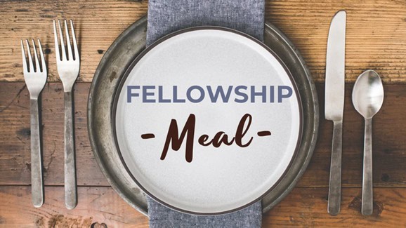 Plate with "Fellowship Meal" text on a table, flanked by two forks on the left and a knife and spoon on the right.