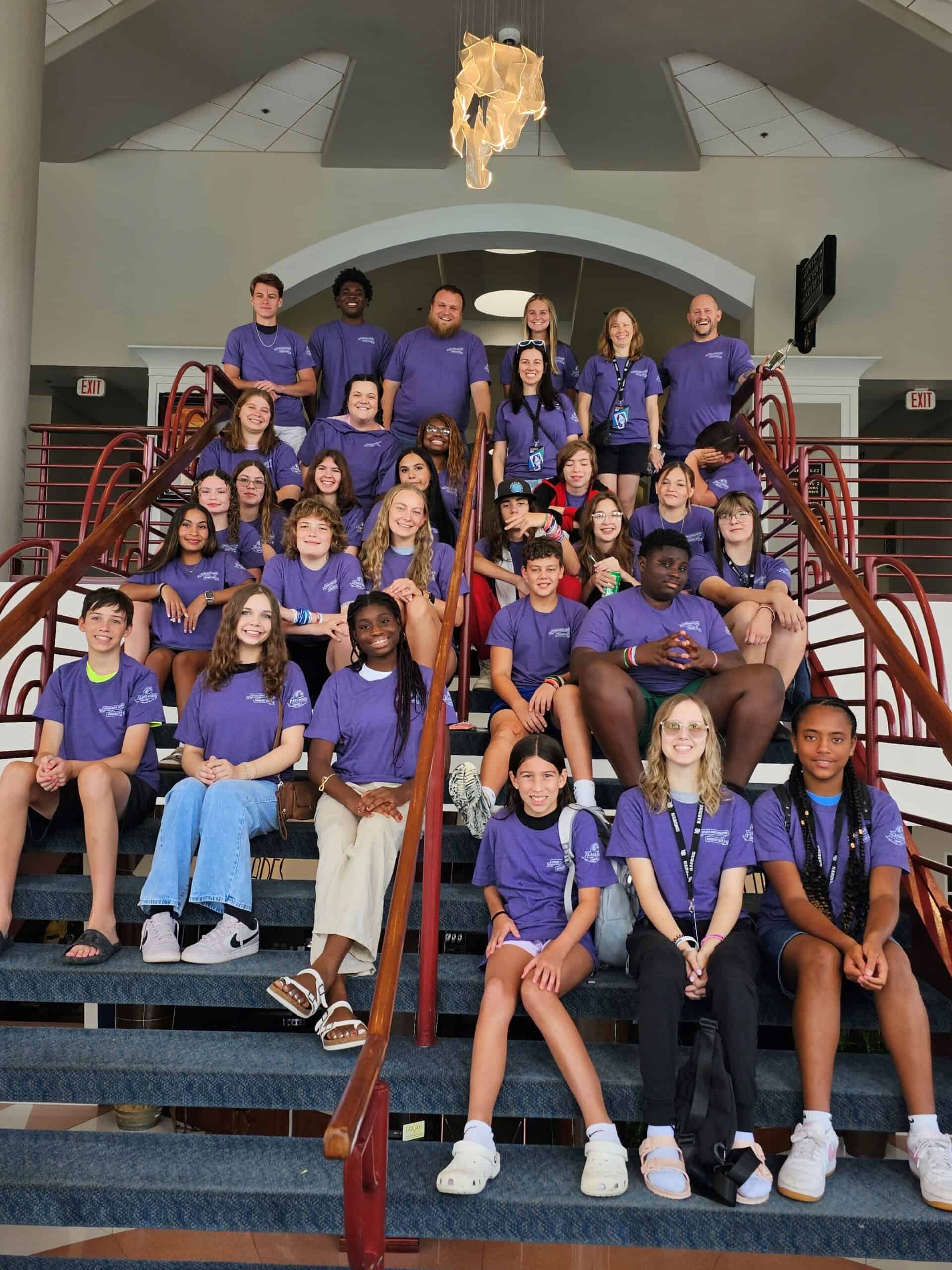 A group of people wearing matching purple shirts pose for a photo on a staircase indoors.